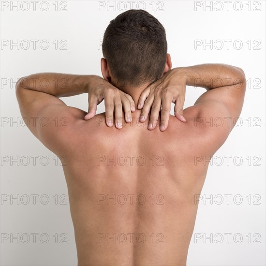 Rear view shirtless man having back pain standing against white wall