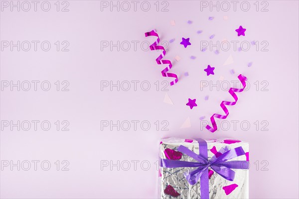 Curled streamers star shape confetti silver gift box against pink background