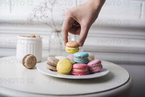 Hand picking up macaroon from white plate kept white table