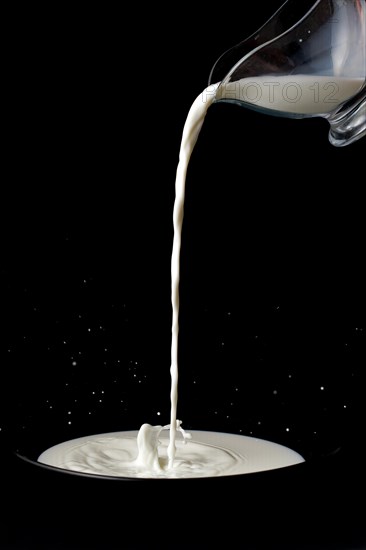 Pitcher with milk pouring on a plate with splash effect on a black background