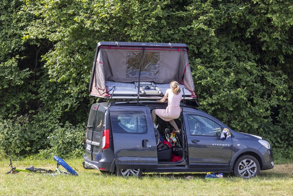 Roof tent on a Dacia Stepway. A young woman struggles to unfold the tent