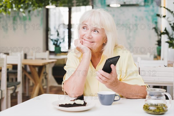 Dreamy smiling elderly woman with smartphone