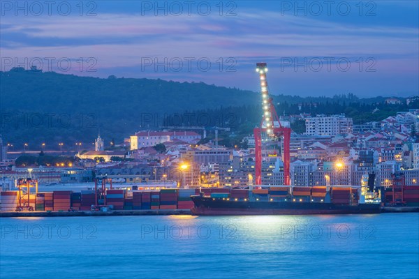 View of Lisbon port with moored sea container ship with port cranes in the evening twilight over Tagus river. Lisbon