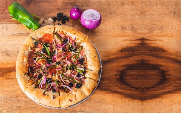 View of supreme pizza with vegetables on wooden background. Top view of supreme pizza with olives and vegetables on wooden table