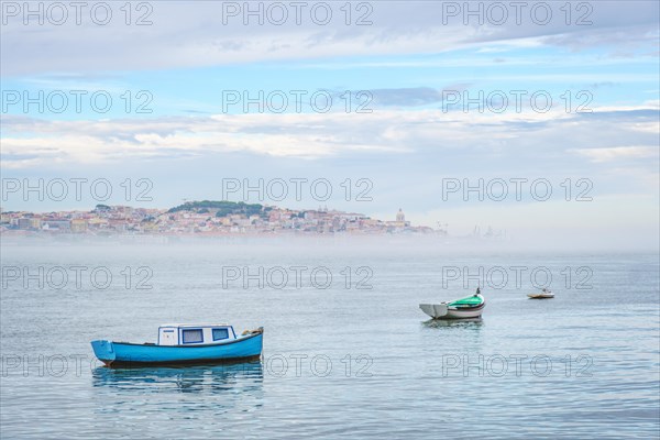 Fishing boats in Tagus river on misty morning with Lisbon in background with miSt Lisbon