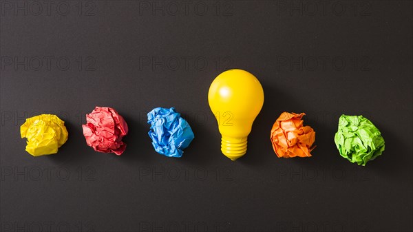 Colorful crumpled paper ball with yellow light bulb against black background