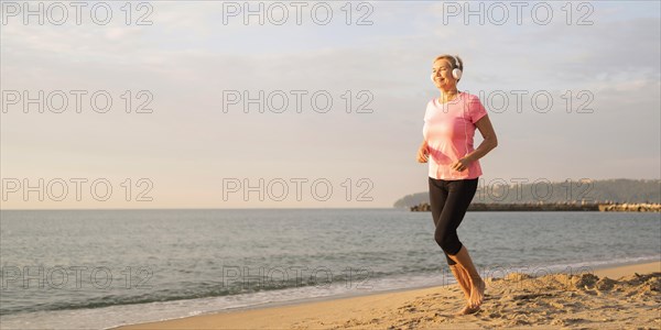 Side view elder woman with headphones jogging beach
