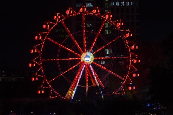 The red lights of the Ferris wheel at the Mainfest shine in the evening. The Mainfest on the Mainkai
