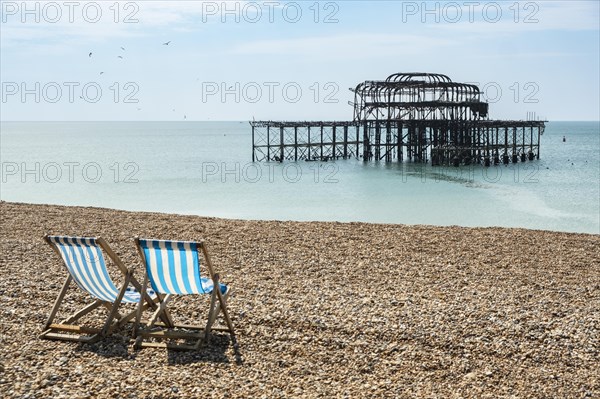 Two folding chairs on the beach in front of the ruins of the burnt down West Pier in Brighton