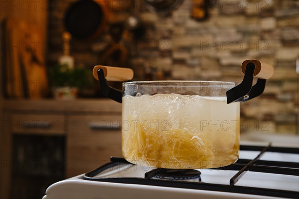 Cooking fettuccine pasta into boiling water in a transparent glass saucepan
