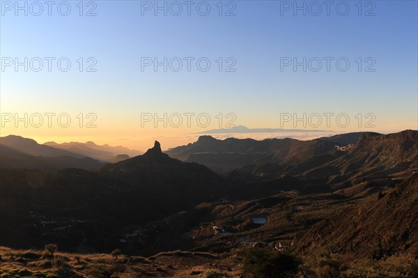View of Roque Nublo on Gran Canaria with the silhouete of the Teide mountain in the background and a sea cloud. Sunset in Gran Canaria. Roque Nublo and El Teide together