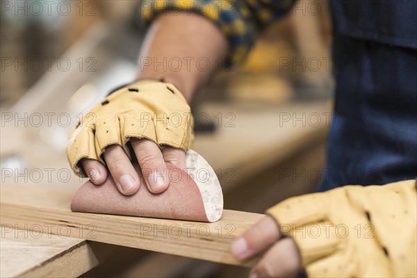 Close up male carpenter rubbing down wood with sandpaper