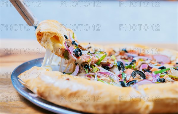 Close-up spatula taking a slice of supreme pizza with vegetables. Hand taking a slice of supreme pizza with spatula