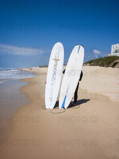 Two surfers standing on the beach behind their surfboards stuck in the sand