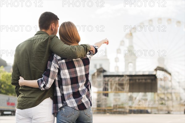 Rear view woman with her boyfriend pointing ferris wheel while