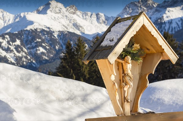 A wooden sculpture of crucified Jesus Christ on the background of the Alps mountains in winter. View of the mountains. Religion and culture. Austria