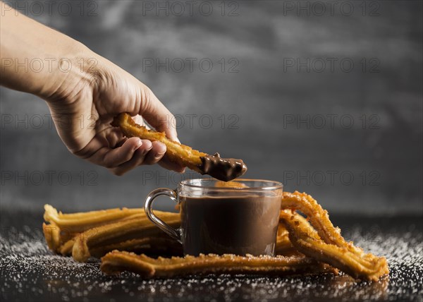 Hand dipping fried churros chocolate front view