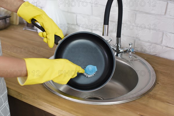 Person hand with yellow glove washing pan with brush kitchen