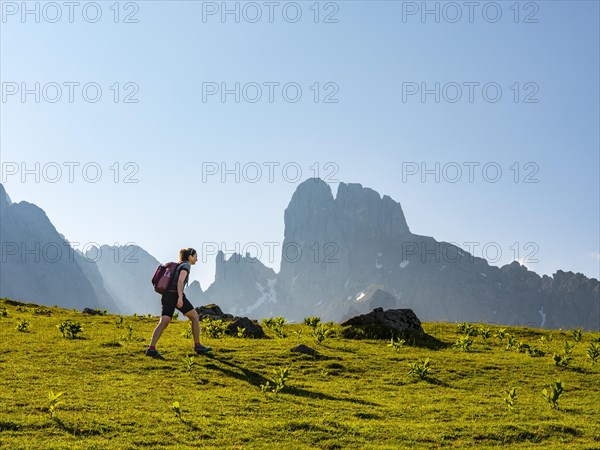 Woman hiking across alpine meadow in front of the peaks of the Bischofsmuetze