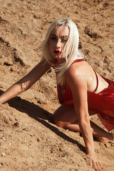 Beautiful blond woman in a red sexy dress on the background of the sky and sand. Beauty of the body and face