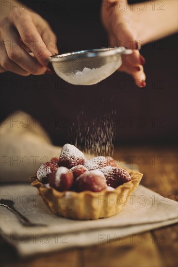 Woman dusting sugar powder strawberry tart