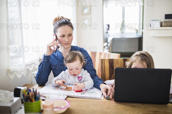 Woman talking smartphone while her children playing desk