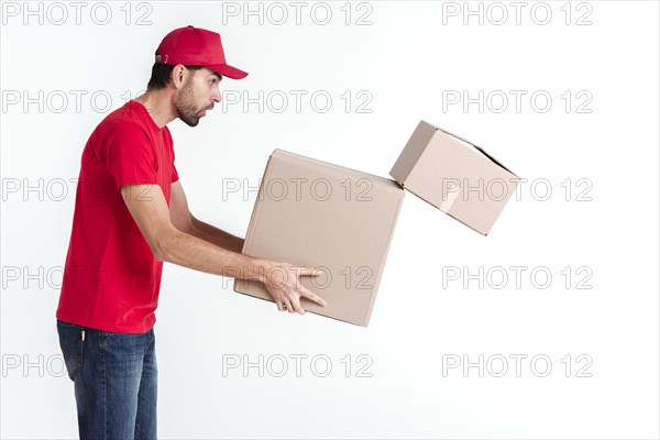 Side view delivery boy holding parcel post boxes drops one