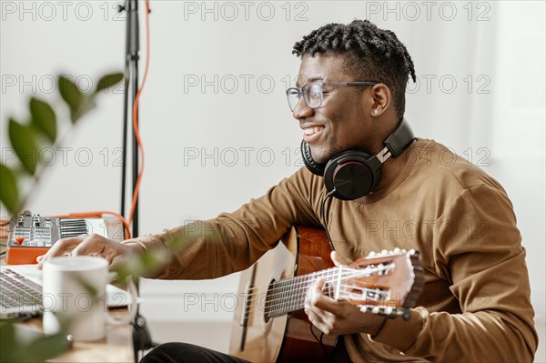 Side view smiley male musician home playing guitar mixing with laptop