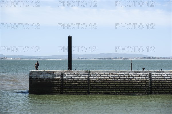 A person sits on a quay wall at the port of Lisbon