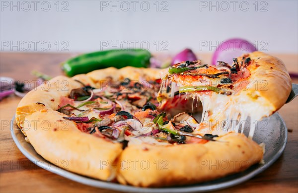Close up of spatula taking a slice of supreme pizza with vegetables. Spatula taking a slice of supreme pizza with spatula