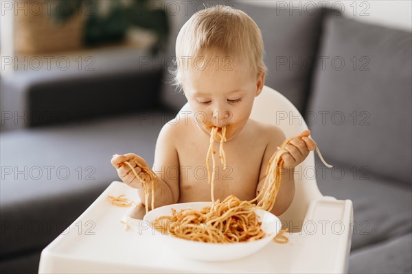 Front view baby boy playing with pasta his highchair