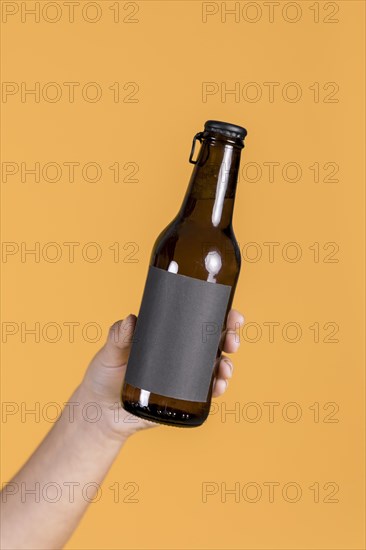 Human hand holding brown beer bottle against yellow wall backdrop