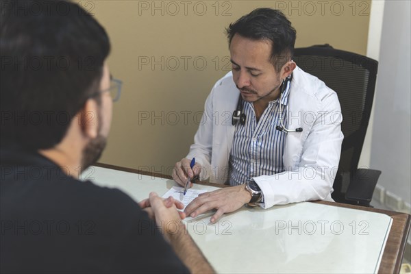 Latin doctor sitting at his desk writing a prescription to his patient