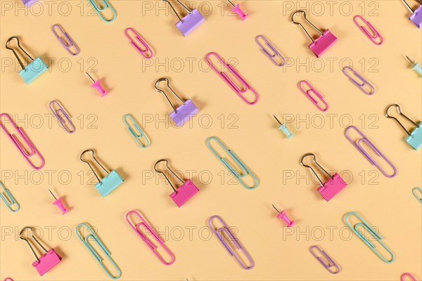 Stationery items like paper clips and drawing pins arranged on side of yellow background