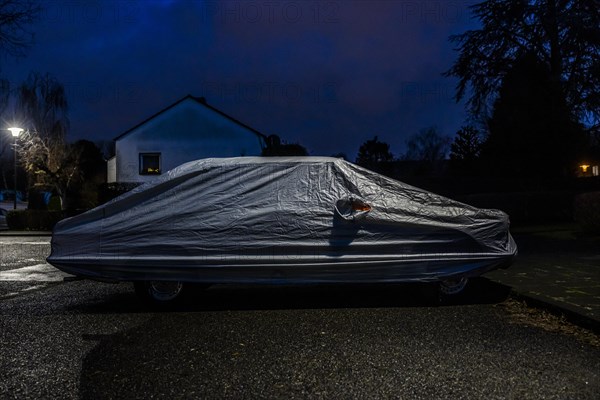 Covered car parked on the street under a lamppost at night