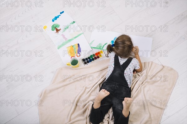 Girl painting by water colors paper lying floor