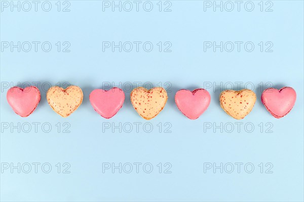 Pink and yellow heart shaped French macaron sweets in a row on blue background