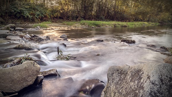 Long exposure of the mountain river in the rays of the setting sun. Water in a raging mountain river. Beautiful natural background of stones and water. Visible river bank. Background to insert a text