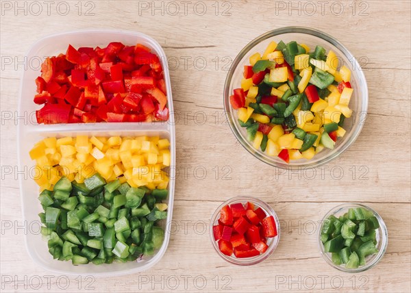 Organic fresh chopped red green yellow bell peppers tiffin box glass bowls wooden desk