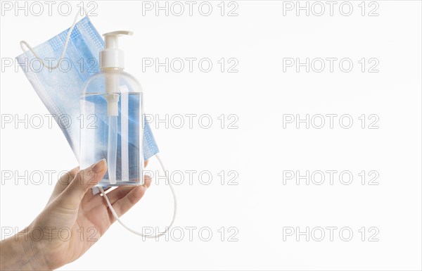 Hand holding medical mask with hand sanitizer bottle