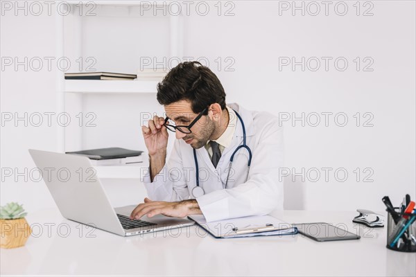 Concentrating young male doctor working laptop clinic