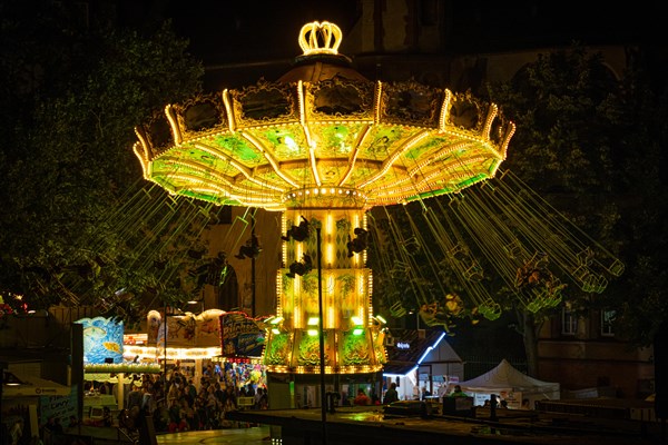 The colourful lights of the carousel at the Mainfest glow in the evening. The Mainfest on the Mainkai