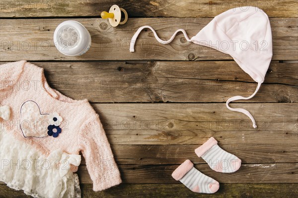 Pink baby s dress with headwear pair socks milk bottle pacifier wooden table