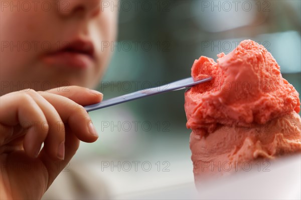 Unrecognizable child eating strawberry ice cream with a spoon