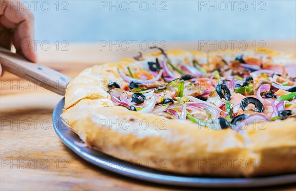 Hand taking a slice of supreme pizza with spatula. Close-up spatula taking a slice of supreme pizza with vegetables