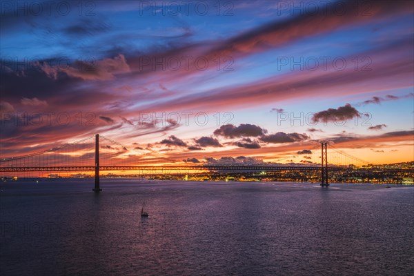 View of 25 de Abril Bridge famous tourist landmark of Lisbon connecting Lisboa and Almada on Setubal Peninsula over Tagus river in the evening twilight with boats. Lisbon