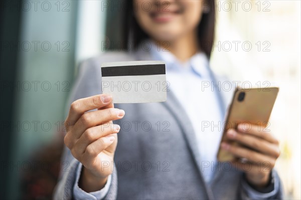 Smiley businesswoman with smartphone credit card outdoors
