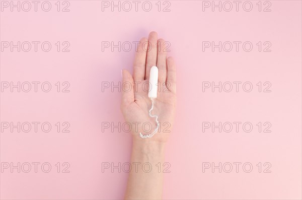 Hand holding tampon pink background