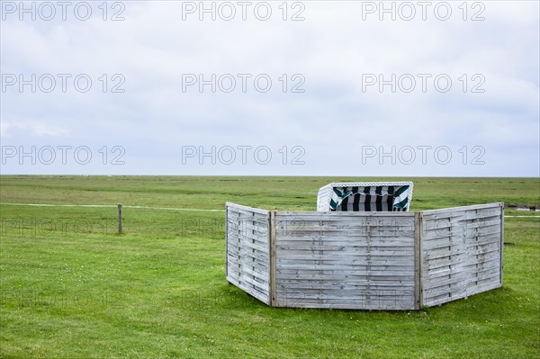 Beach chair in a meadow on the Wadden Sea with windbreak in front of it