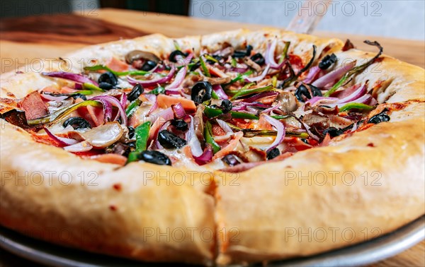 Close-up of supreme pizza and olives served on wooden table. Delicious supreme pizza and pepperoni on the table